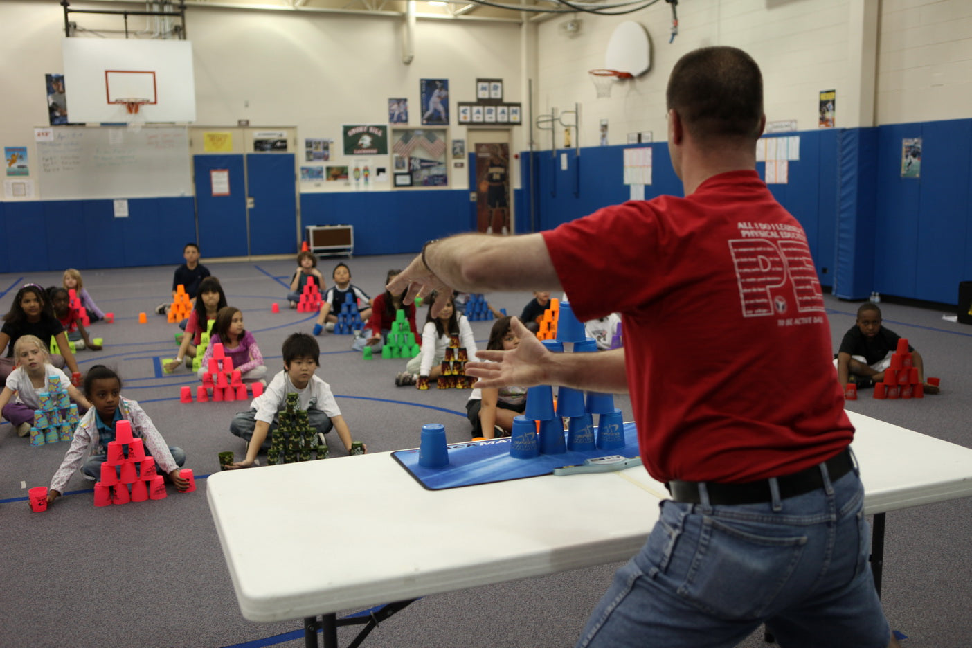 PE teacher demonstrating sport stacking to a class of students in a school gymnasium